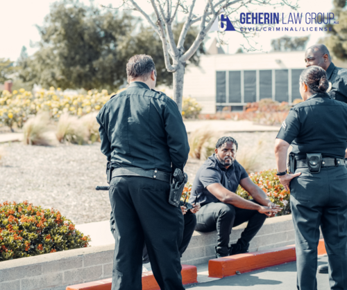 Two men being questioned by police, sitting on a curb.
